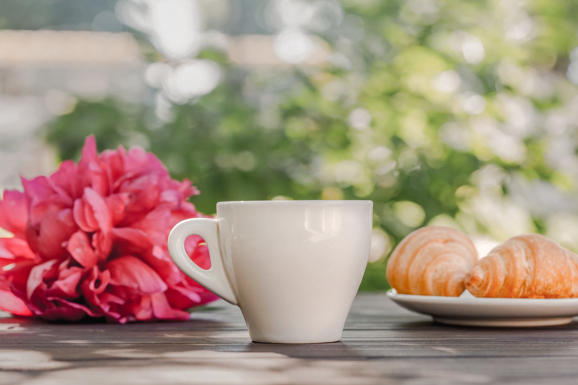 Gedeckter Frühstückstisch mit Kaffee, Croissant und Blumen